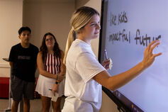 A student writes on an electronic whiteboard as two other students look on.